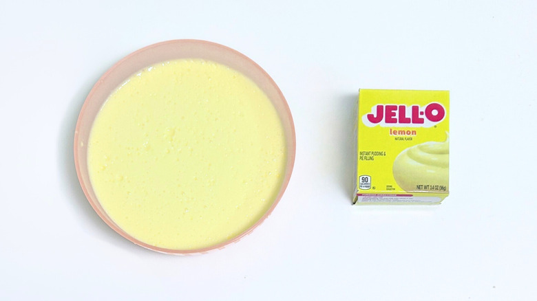 A bowl of pale yellow pudding next to a box of Jell-O Lemon Pudding Mix