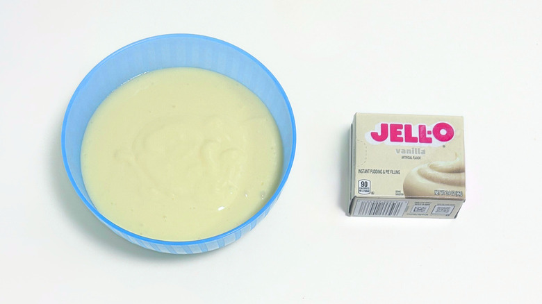 A bowl of pale yellow pudding next to a box of Jell-O Vanilla Pudding Mix