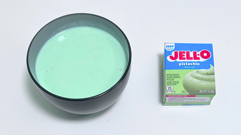 A bowl of teal-colored pudding next to a box of Jell-O Zero Sugar Pistachio