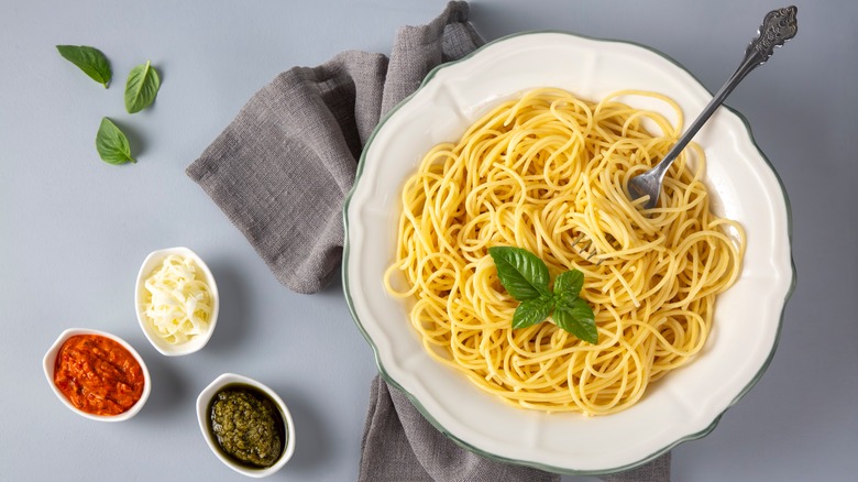 White bowl with cooked spaghetti and a trio of different sauces