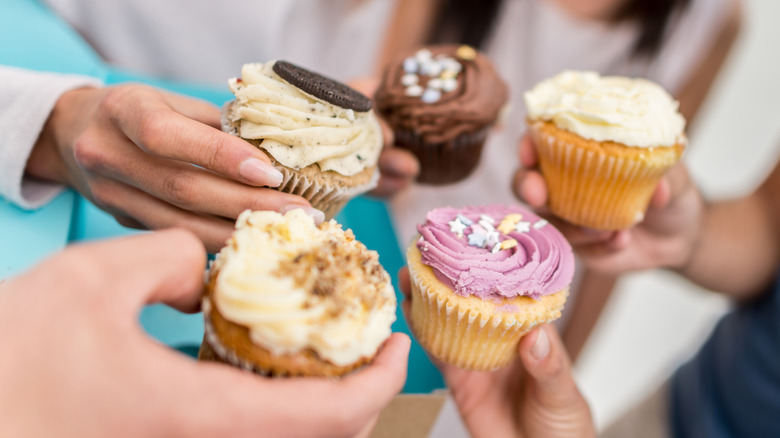 hands holding cupcakes out