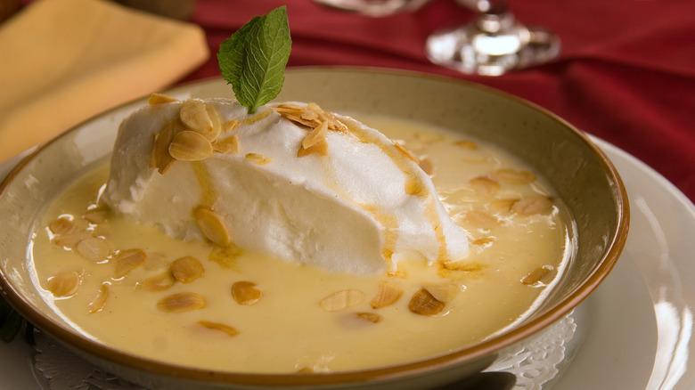 Floating island dessert in tan bowl topped with toasted almonds and fresh mint