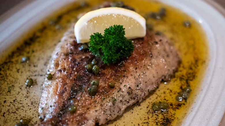 Close-up of sole meunière served on a white platter and garnished with a lemon wedge and parsley sprig