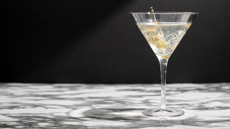 Close-up of a martini in a martini glass garnished with olives on a countertop