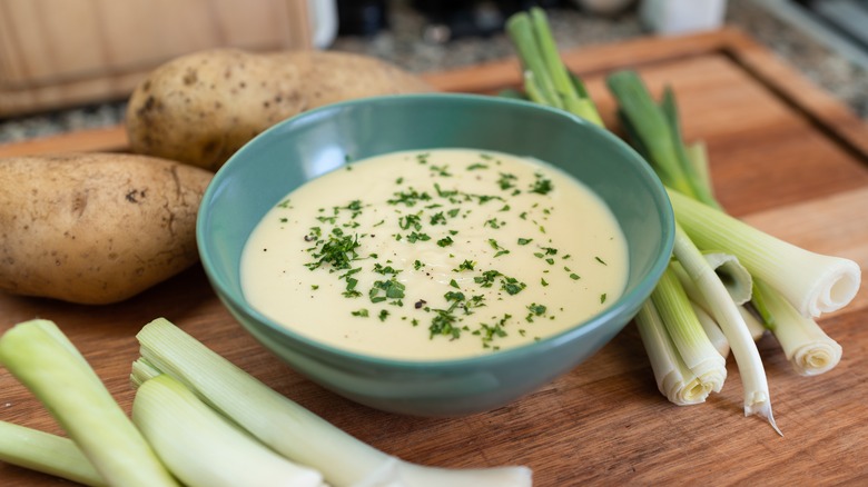 Blue bowl of vichyssoise garnished with chives and surrounded by potatoes and leeks