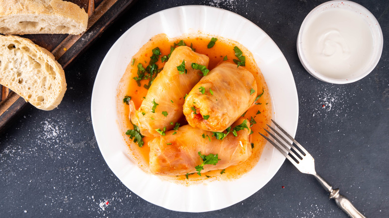a plate of stuffed cabbage rolls over a sauce and slices of bread on the side