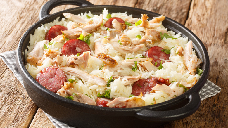 a cast iron bowl of chicken bog with pieces of chicken, sausage, and parsley sticking up on top