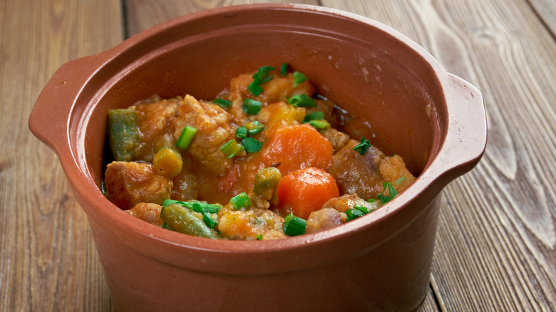 stew with meat, carrots, green beans, and green onions in a crock on a wooden table