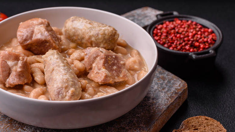 a bowl of beans in sauce with big chunks of pork on top and a bowl of red berries on the side