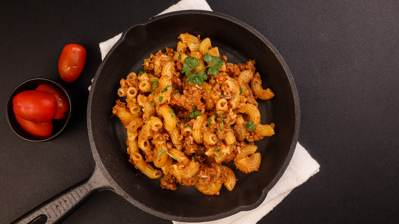 a cast iron skillet full of Slumgullion or goulash with Roma tomatoes in a side bowl