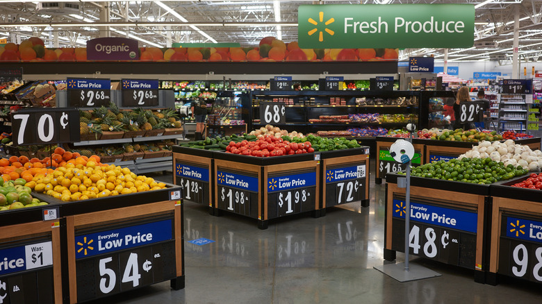 The fresh produce section of a walmart supermarket with tomatoes, limes, lemons, oranges, cucumbers, apples, pineapples, and onions on display
