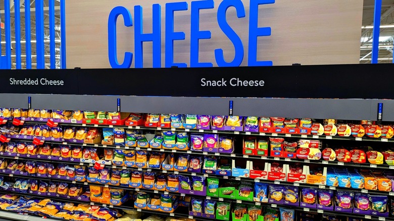 The cheese aisle at a walmart store displaying a variety of sliced, shredded, snack, and block cheeses for sale