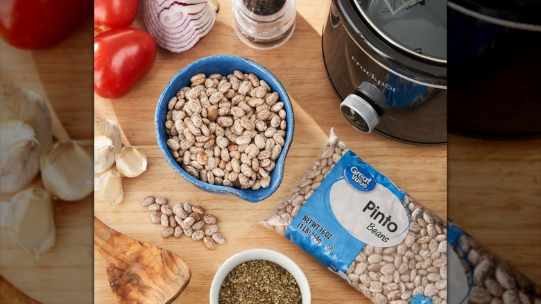 A bag of walmart great value dried pinto beans on a kitchen counter with a crockpot and other ingredients