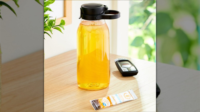 A packet of great value energy peach mango drink mix sits next to a reusable water bottle full of a yellow beverage made with the energy mix