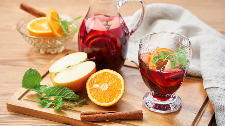 Pitcher and glass filled with homemade sangria, with oranges and apples scattered around