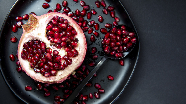 Halved pomegranate and seeds on black plate