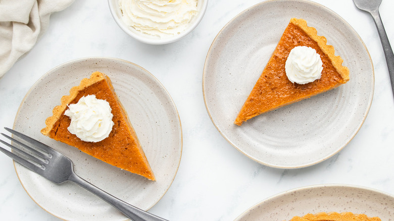 Two slices of Southern-Style Sweet Potato Pie on white plates with whipped cream