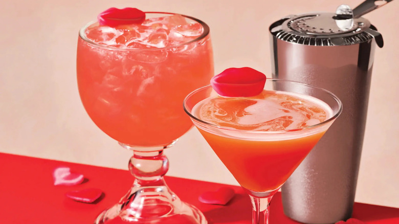 Two pink-hued Applebee's cocktails, garnished with red lip-shaped gummies, next to a cocktail shaker.