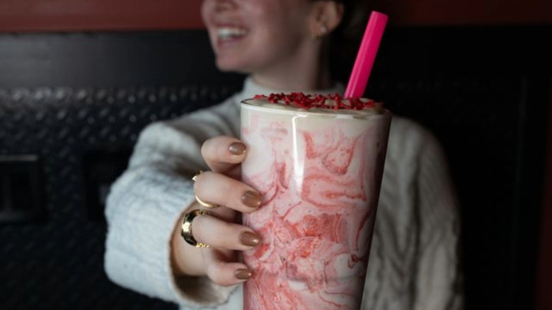 A woman holds a a milkshake with red swirls in a glass.