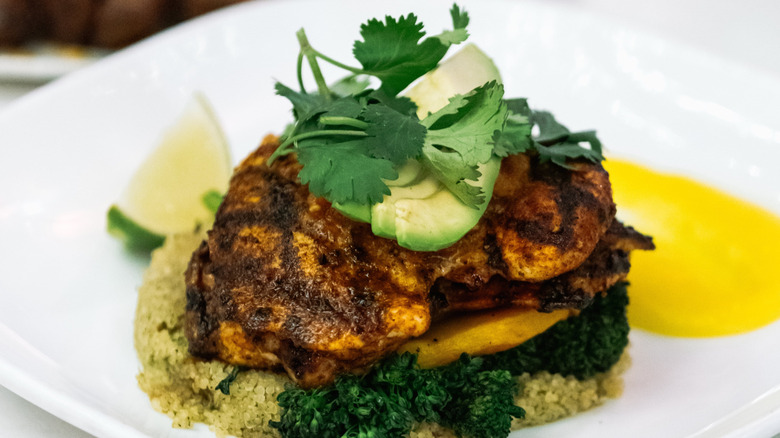 Grilled chicken thighs served over greens and quinoa and topped with avocado and cilantro on a plate.