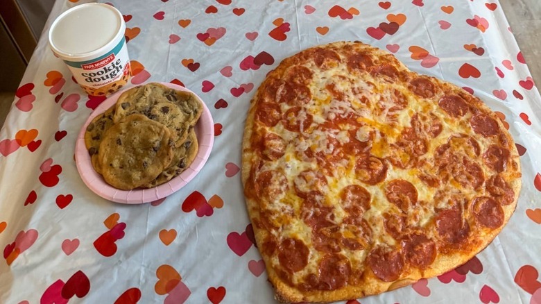 A Papa Murphy's heart-shaped pizza with a plate of cookies and a tub of cookie dough.