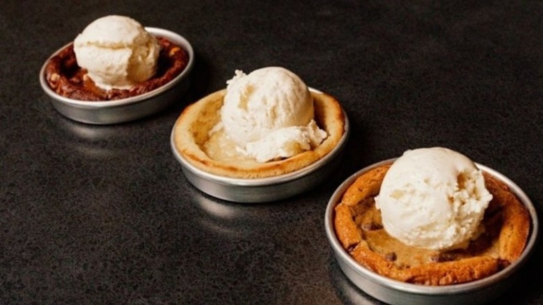 Three ice cream-topped cookies in mini pans on a gray table.