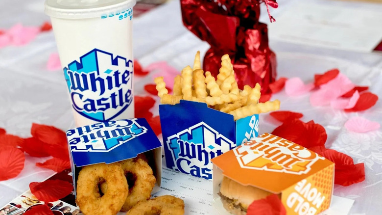 A White Castle meal of burger, fries, onion rings, and a drink, on a table covered with rose petals.