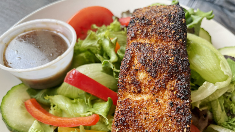 Blackened fish on a salad next to dressing