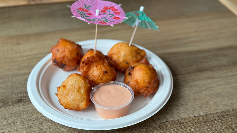 Conch fritters on a white plate with dipping sauce and tiny umbrella