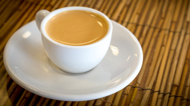 A white cup of Cuban coffee against a bamboo surface