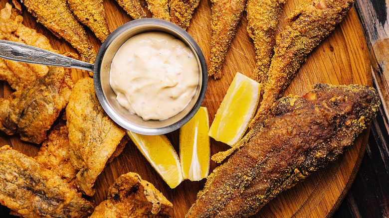 Fried mullet with dipping sauce and lemon wedges on a wooden serving tray