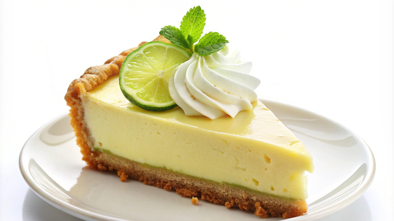 Slice of Key lime pie on a white plate with lime and whipped cream on top