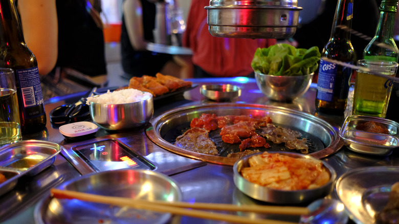 Korean food on the grill with kimchi, rice, and beer at the table
