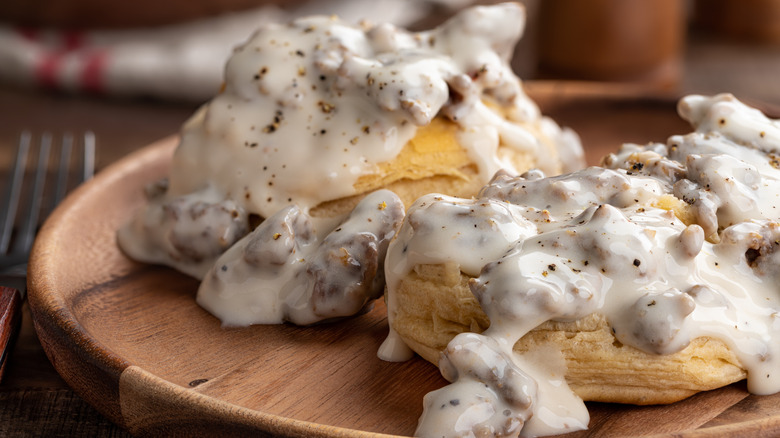 A wooden plate of biscuits and sausage gravy