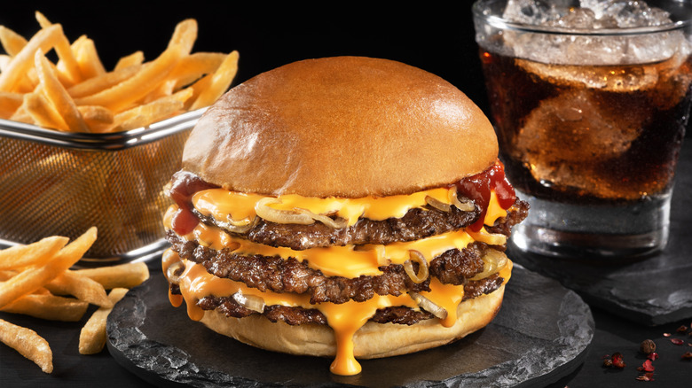 A triple cheeseburger with bacon, with a side of fries and a glass of cola