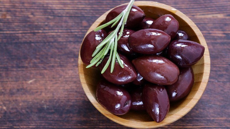 Wooden bowl filled with kalamata olives and a sprig of rosemary