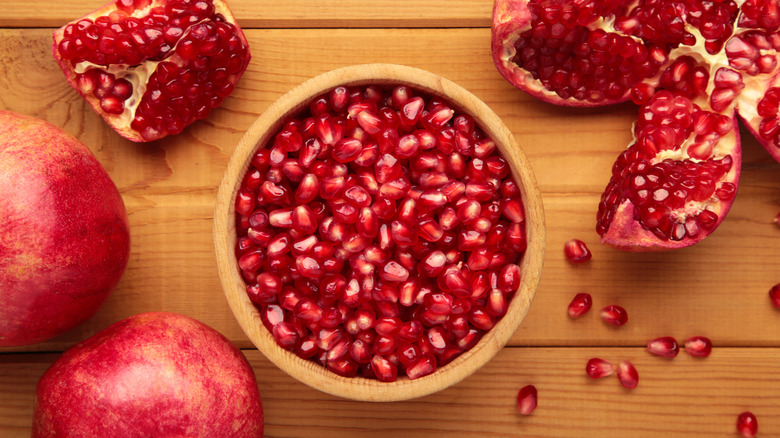 Whole pomegranates and pomegranate seeds in a wooden bowl