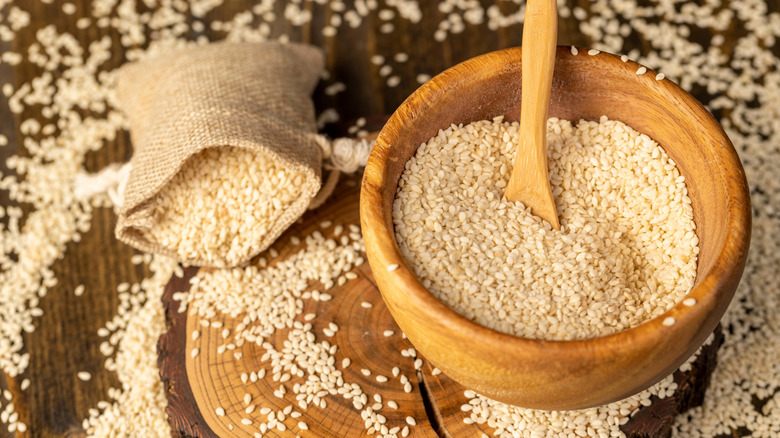 Whole white sesame seeds in wooden bowl and burlap sack