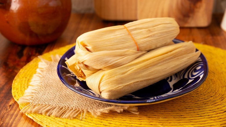 Tamales, similar to bvnaha, still wrapped and stacked on a blue plate