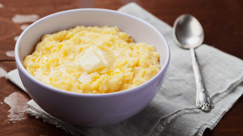 Cornmeal mush with a pat of melting butter, in a bowl beside a spoon on a napkin