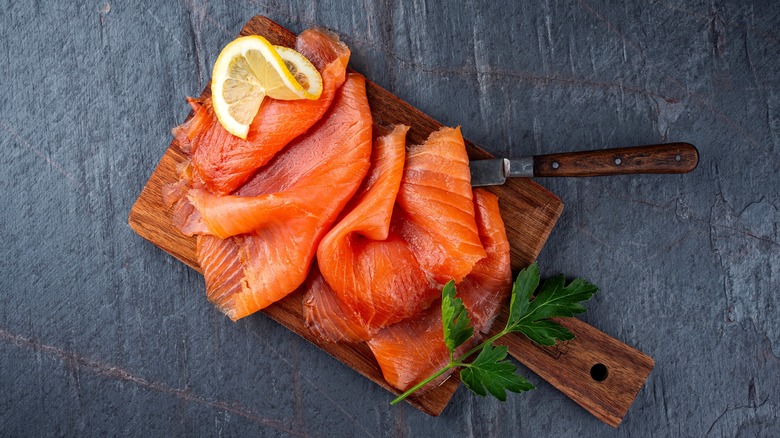 Rich orange smoked salmon on a wooden cutting board, with a slice of lemon and sprig of parsley