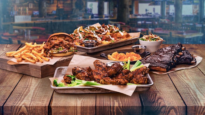 Twin Peaks burger, chicken wings, ribs, and nachos dishes on wooden table with restaurant background