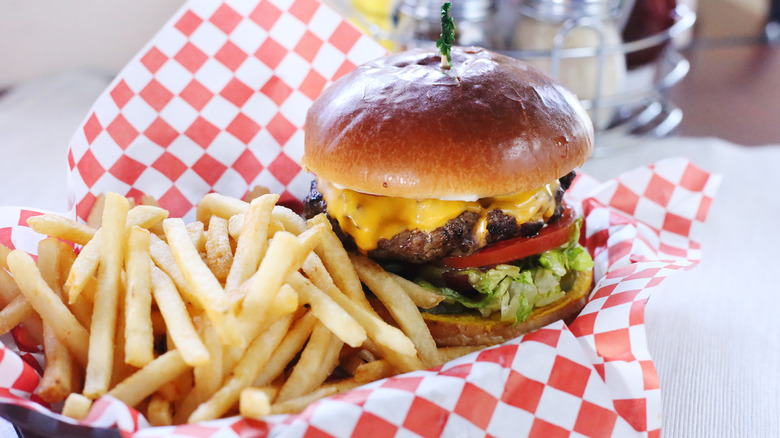 Cheeseburger with lettuce and tomato in basket with fries and checkered paper on diner table