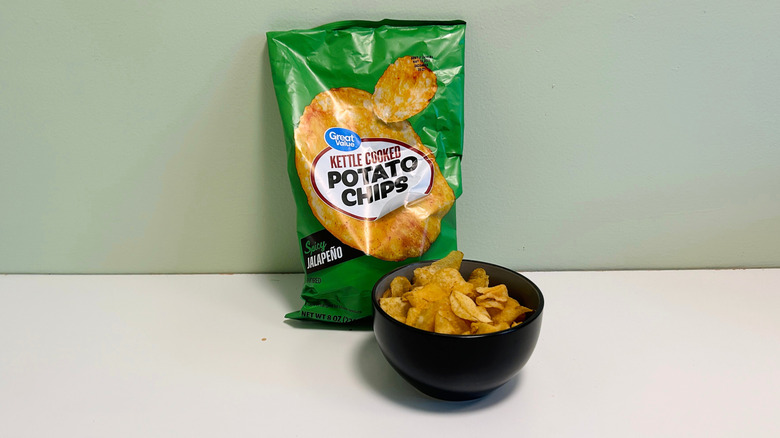 A bag of Great Value Kettle Cooked Potato Chips behind a black bowl of chips