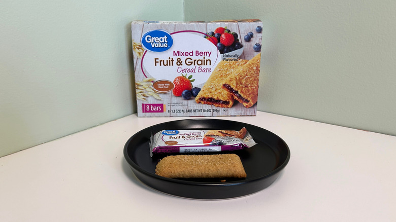A box of Great Value mixed berry fruit and grain cereal bars beside a cereal bar on a black plate