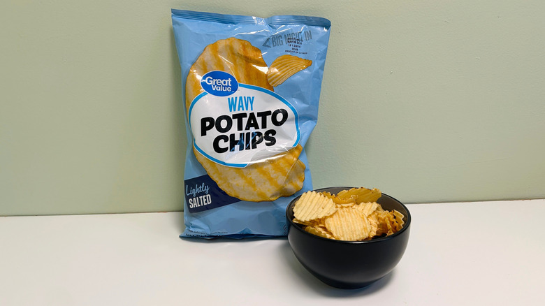 A bag of Great Value Wavy Potato Chips behind a black bowl of chips