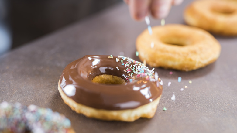 Person dropping sprinkles on frosted donut