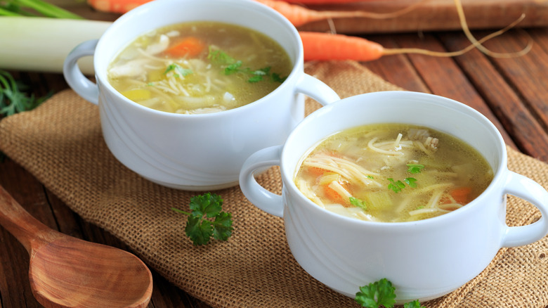 Two cups of homemade chicken noodle soup on burlap towel