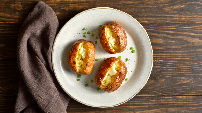 Three oven-baked potatoes on a white plate garnished with butter and green onions