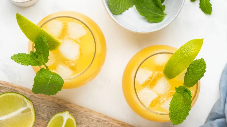 Two yellow mai tai cocktails, with ice and garnished with mint leaves and lime wedges